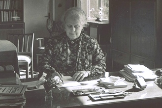 Schwarz-weiss Foto: Helene Weber sitzt an ihrem Schreibtisch und schreibt