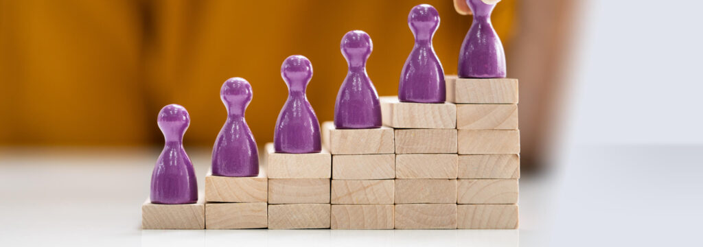 Symbolbild: Gleichstellung auf dem Arbeitsmarkt Holztreppe mit Spielfiguren auf jeder Stufe