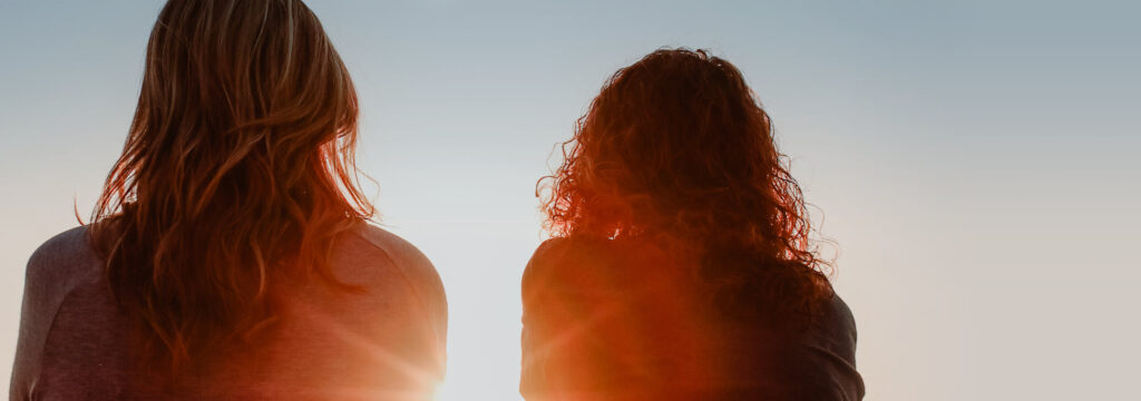 Symbolbild Frauengesundheit: 2 Frauen stehen im Sonnenuntergang mit dem Rücken zur Kamera